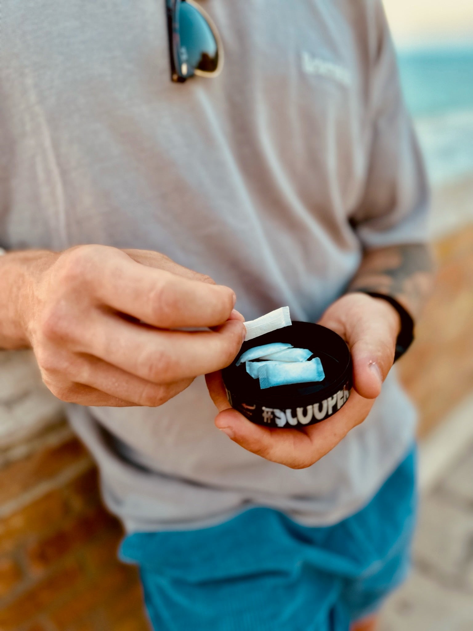 Ein Mann hält eine offene Dose SCOOPER Energy in der Hand und nimmt sich einen Pouch aus der Dose. Man sieht nur seinen Oberkörper und die Dose steht im Vorergrund des Bildes.