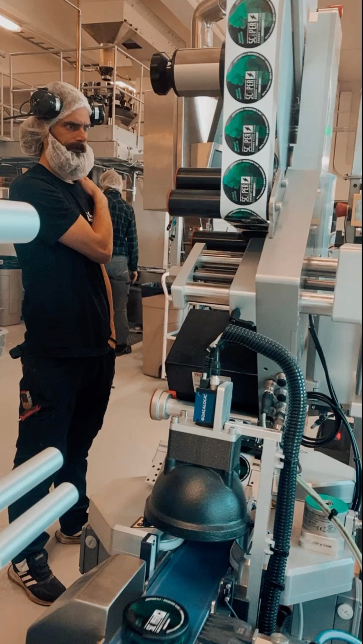 Einblick in die Produktion in Schweden. Man sieht einen Mann mit Haar- und Bartnetz, der die Produktion der SCOOPER Energy Fresh Mint Dosen beaufsichtigt. Die Dosen werden auf einer Maschine gelabelt.