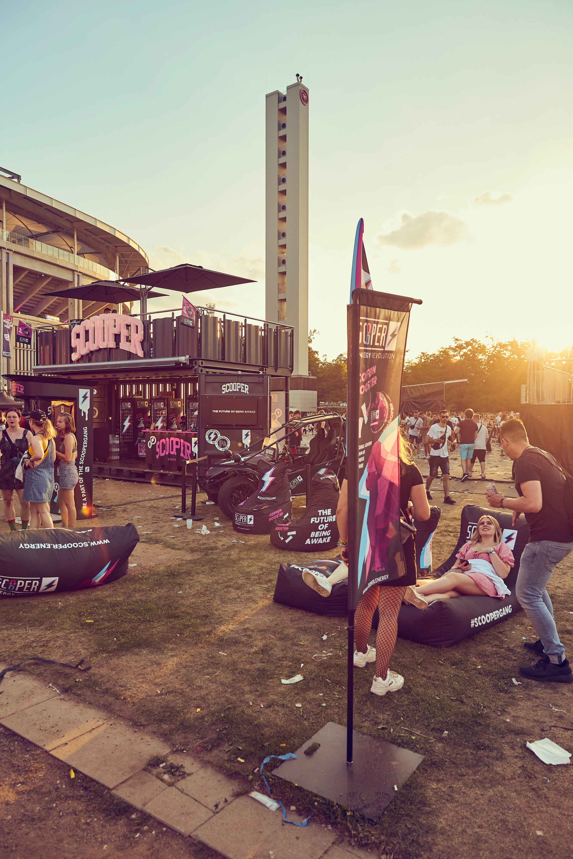 Man sieht den Scooper Stand auf dem World Club Dome 2022 in Frankfurt. Im Hintergrund geht die Sonne unter und im Vordergrund sieht man feiernde Festivalbesucher.
